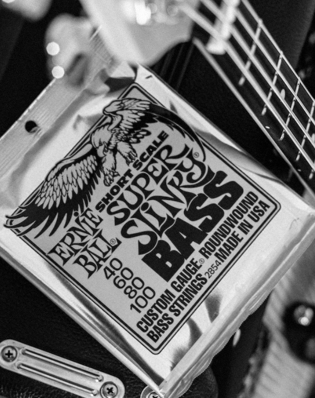 Packet of Ernie Ball Slinky strings on-top of an amp, next to a bass.
